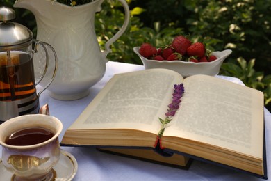 Books, tea and fresh strawberries on table in garden