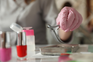 Photo of Professional manicurist with nippers at table in beauty salon, closeup