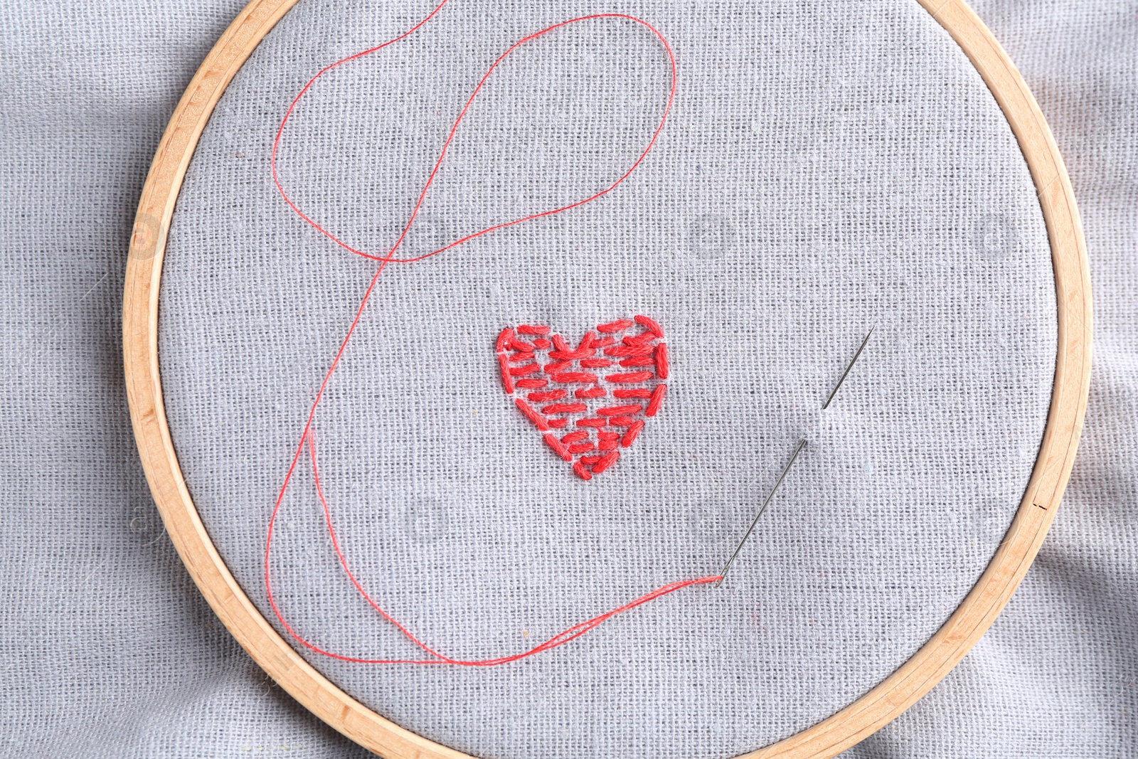 Photo of Embroidered red heart and needle on gray cloth, top view