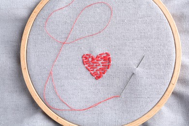 Photo of Embroidered red heart and needle on gray cloth, top view