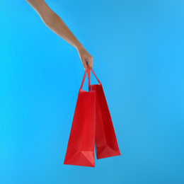 Woman with paper shopping bags on light blue background, closeup