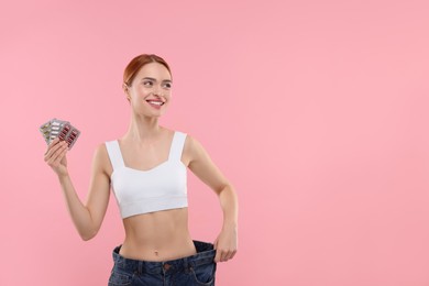 Photo of Slim woman in big jeans with pills on pink background, space for text. Weight loss