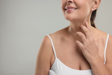 Mature woman touching her neck on grey background, closeup. Space for text