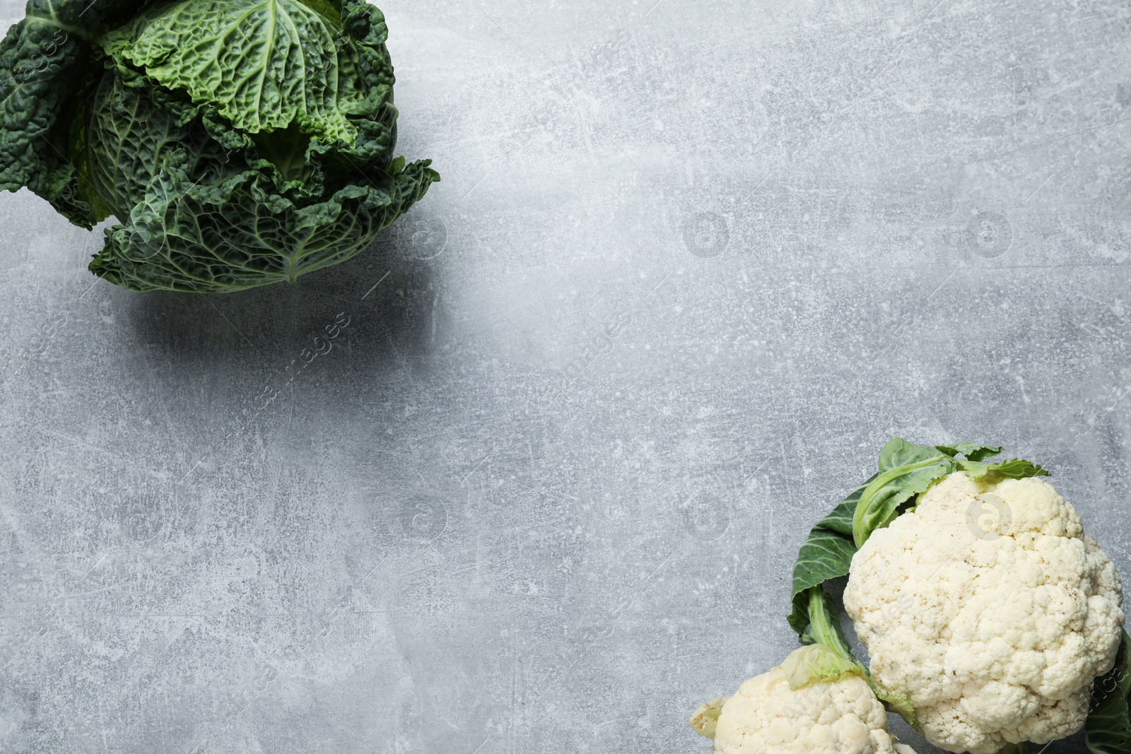 Photo of Fresh ripe savoy cabbage and cauliflower on grey table, flat lay. Space for text