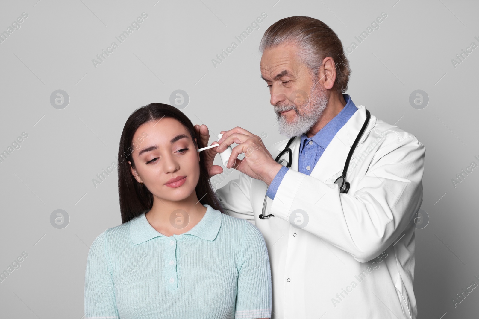 Photo of Doctor spraying medication into woman's ear on light grey background