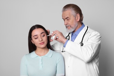 Photo of Doctor spraying medication into woman's ear on light grey background