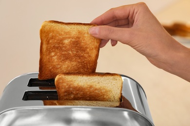Photo of Woman taking slice of bread from toaster against blurred background, closeup