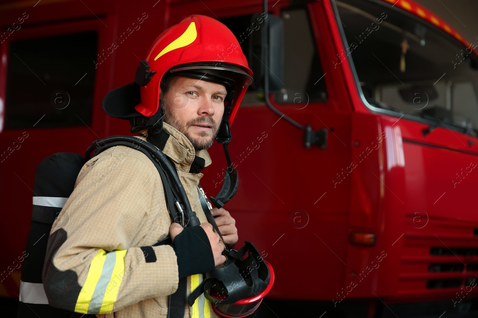 Photo of Portrait of firefighter in uniform near red fire truck at station