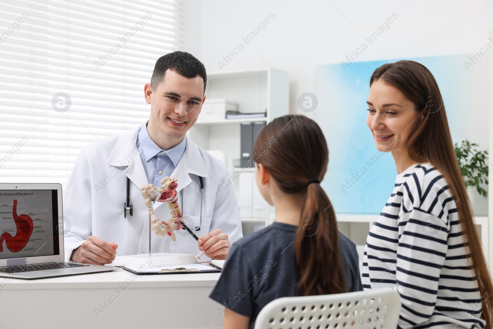 Photo of Gastroenterologist with model of intestine consulting woman and her daughter in clinic