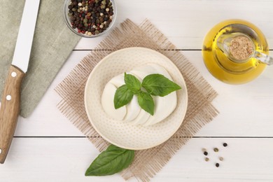 Flat lay composition with tasty mozzarella and basil leaves on white wooden table