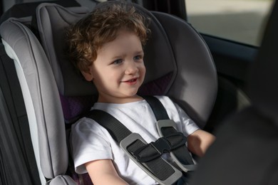 Photo of Cute little boy sitting in child safety seat inside car