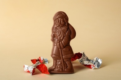 Photo of Sweet chocolate Santa Claus candy and pieces of foil wrapper on beige background