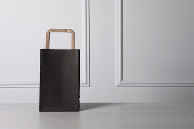 Black paper bag on white wooden table, space for text