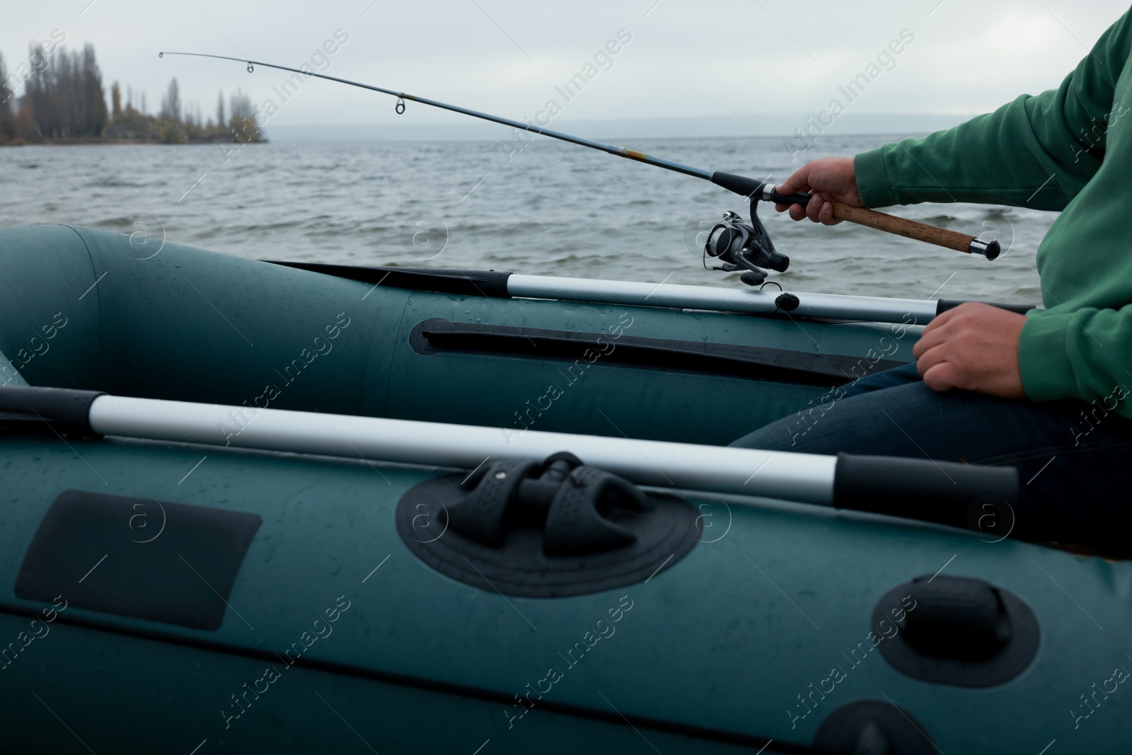 Photo of Man fishing with rod from inflatable rubber boat on river, closeup