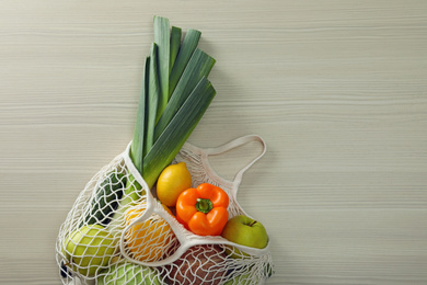 Net bag with vegetables and fruits on wooden table, top view. Space for text