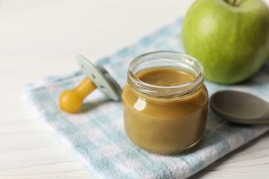 Photo of Jar with healthy baby food, apple, pacifier and spoon on white wooden table