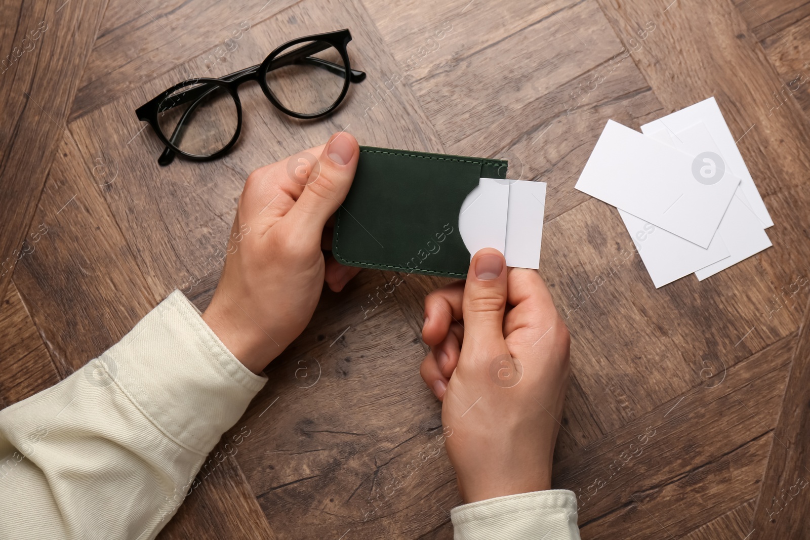 Photo of Man holding leather business card holder with blank cards at wooden table, top view