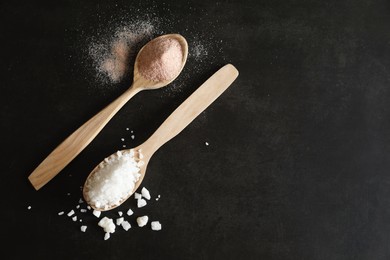 Photo of Different types of organic salt in spoons on black table, flat lay. Space for text