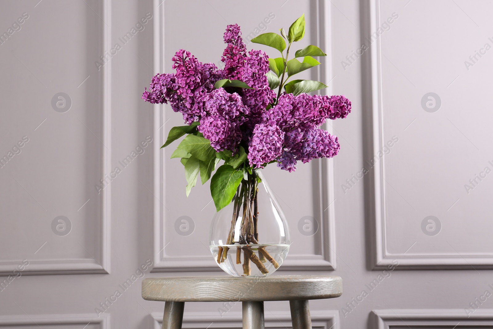 Photo of Beautiful lilac flowers in vase on wooden table near light wall