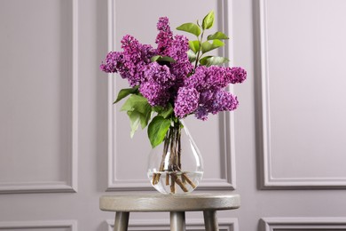 Photo of Beautiful lilac flowers in vase on wooden table near light wall