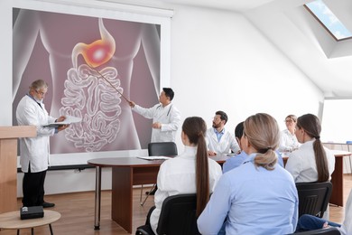 Image of Lecture in gastroenterology. Conference room full of professors and doctors. Projection screen with illustration of digestive tract