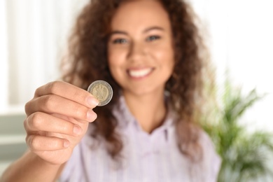 Photo of Happy African-American woman holding coin indoors, focus on hand