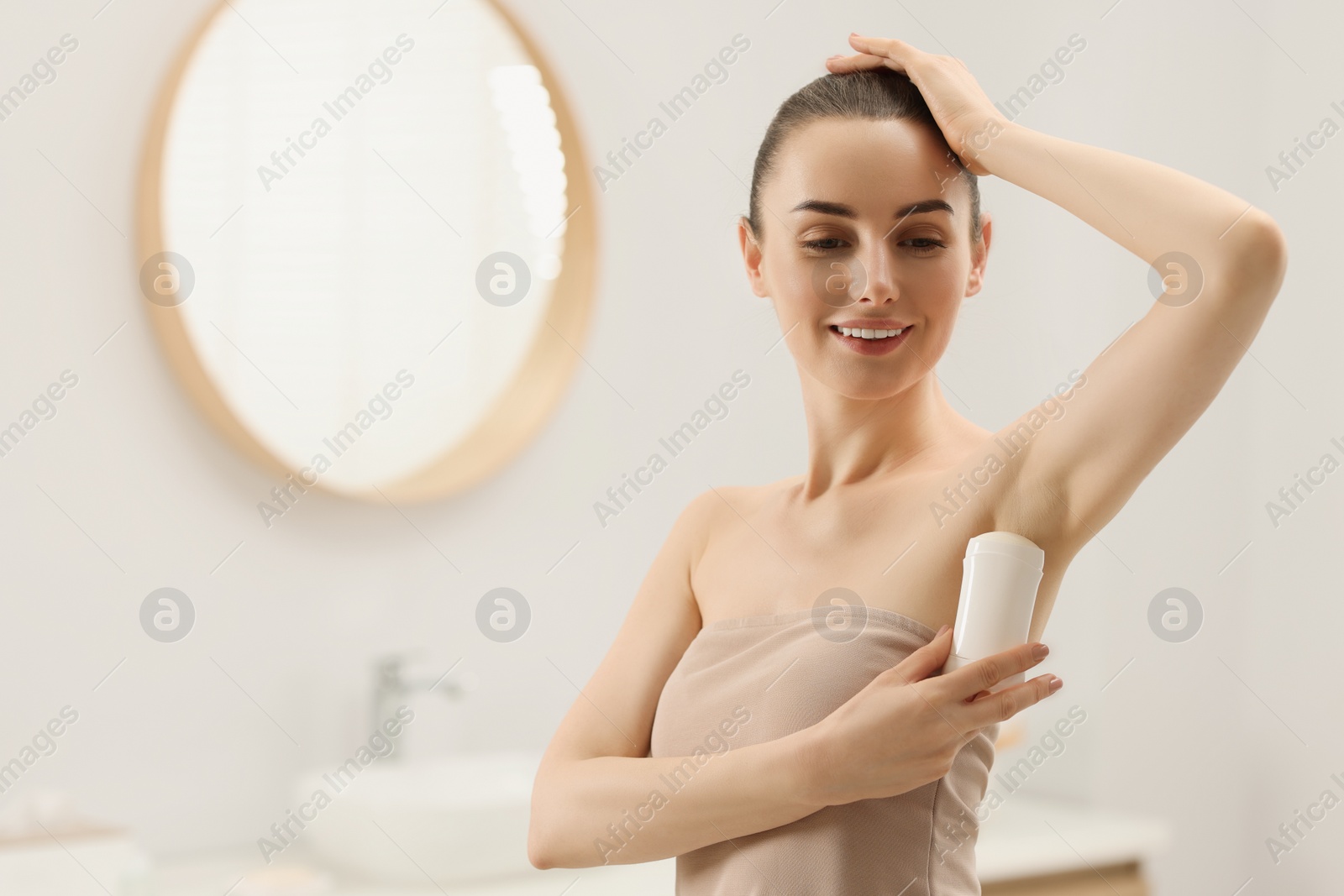 Photo of Beautiful woman applying deodorant in bathroom, space for text