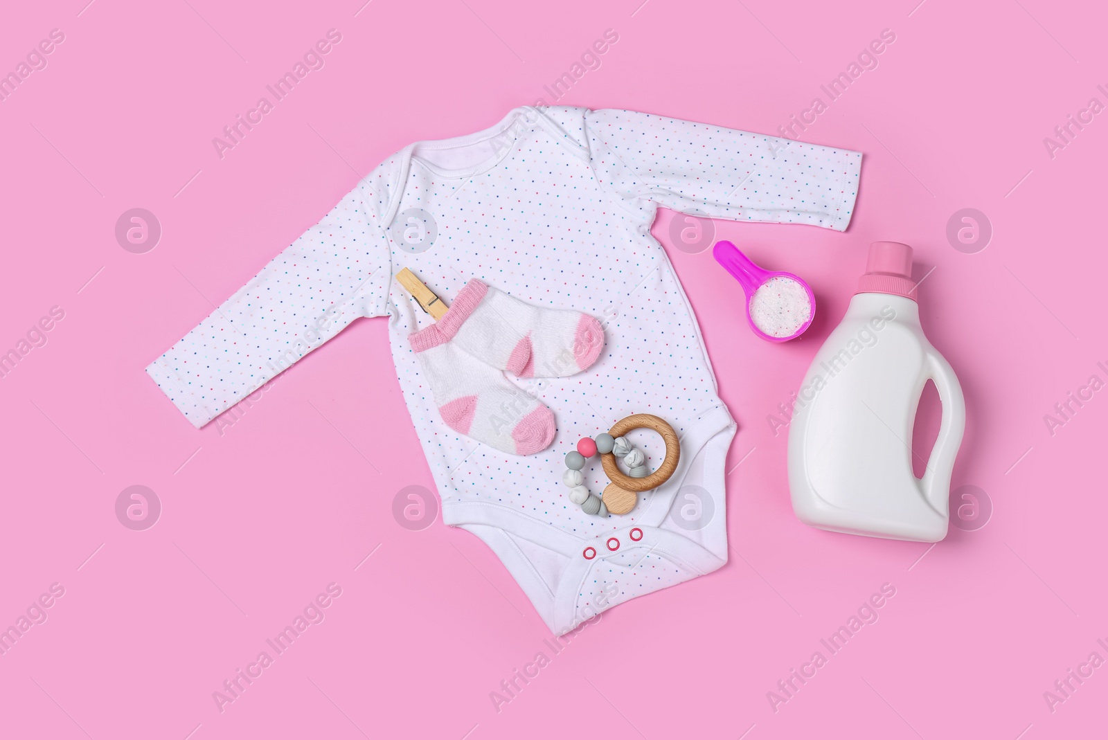 Photo of Flat lay composition with bottle of detergent and children's clothes on pink background