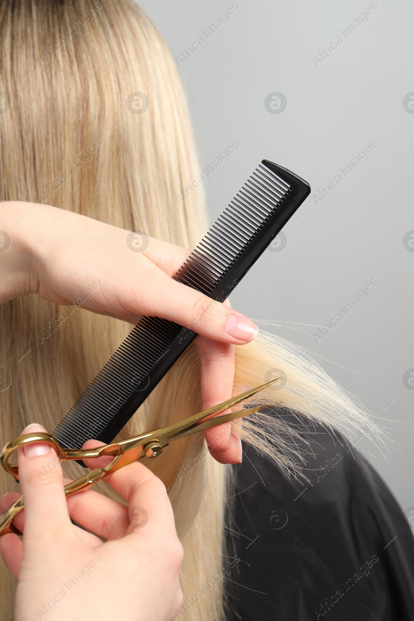 Photo of Hairdresser cutting client's hair with scissors on light grey background, closeup