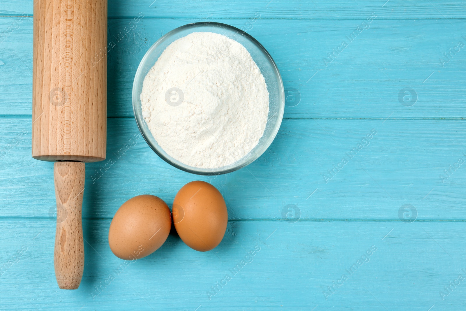 Photo of Raw eggs, flour and rolling pin on light blue wooden table, flat lay. Baking pie