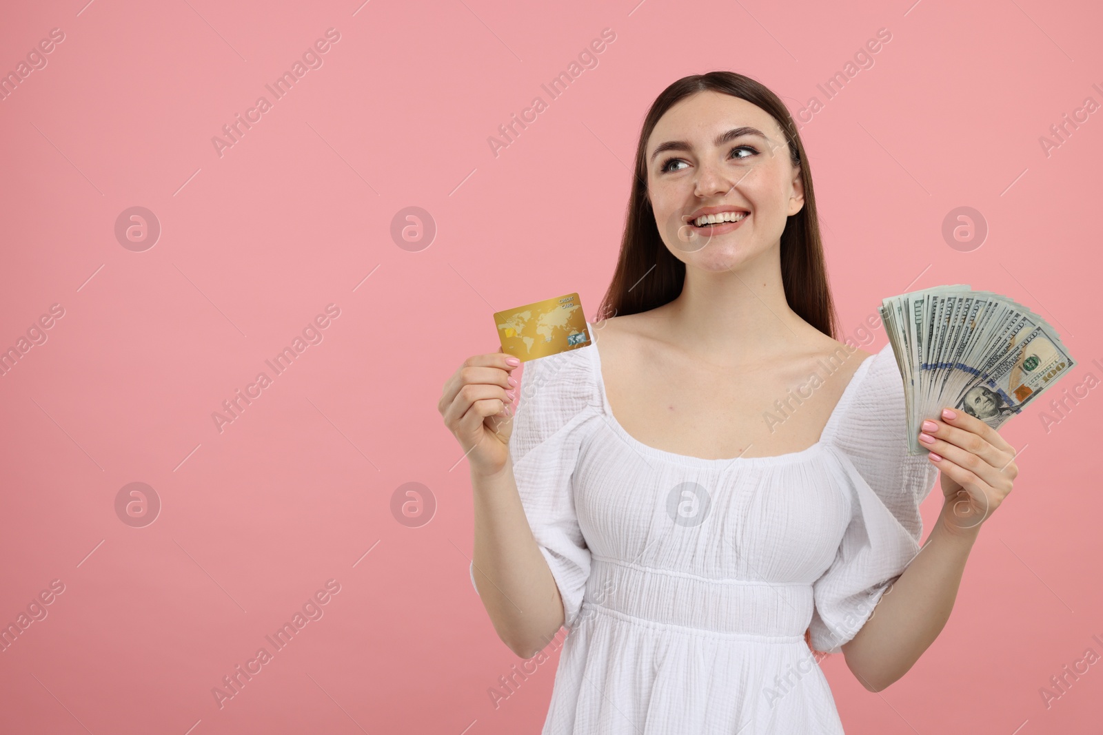 Photo of Happy woman with credit card and dollar banknotes on pink background