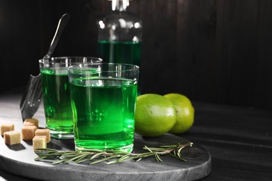 Photo of Absinthe in glasses, rosemary, brown sugar and lime on black wooden table, space for text. Alcoholic drink