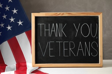 Photo of Blackboard with phrase Thank You, Veterans and American flag on white wooden table. Memorial Day