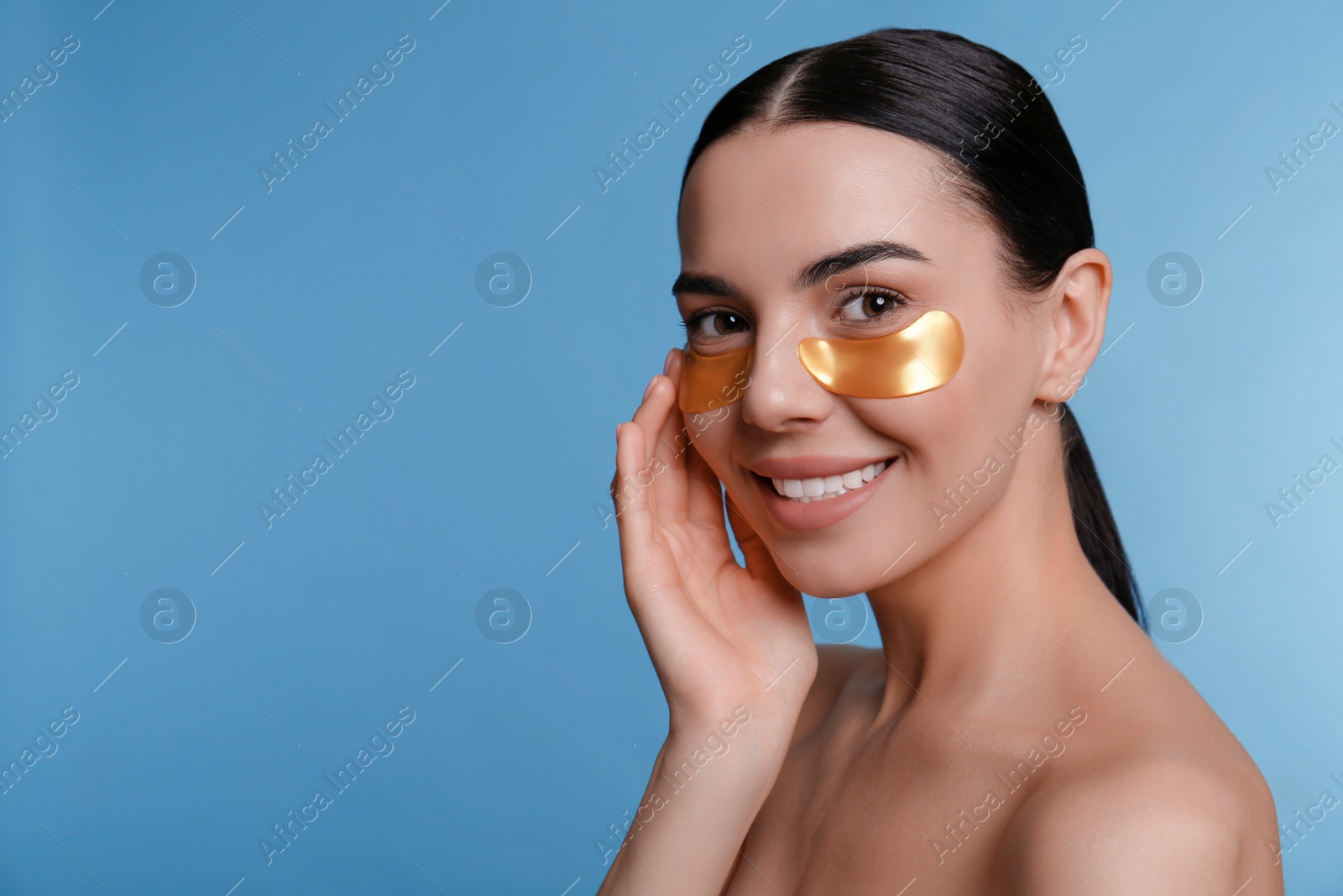 Photo of Beautiful young woman with under eye patches on light blue background, space for text