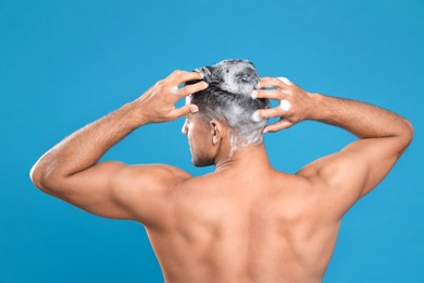 Handsome man washing hair on light blue background, back view