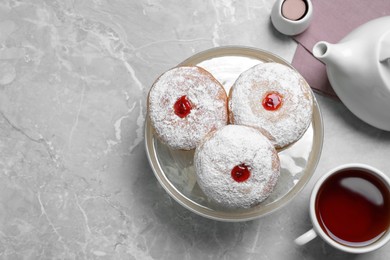 Delicious jelly donuts served with tea on grey table, flat lay. Space for text