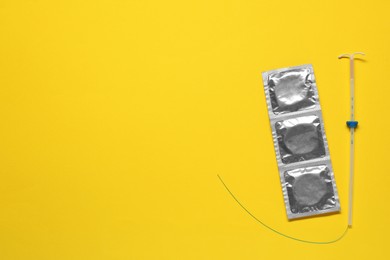 Photo of Contraception choice. Condoms and intrauterine device on yellow background, flat lay. Space for text