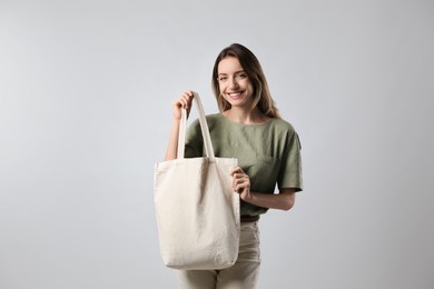 Photo of Happy young woman with blank eco friendly bag on light background