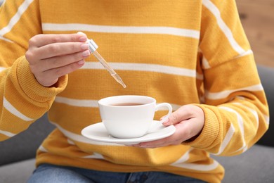 Woman dripping food supplement into cup indoors, closeup