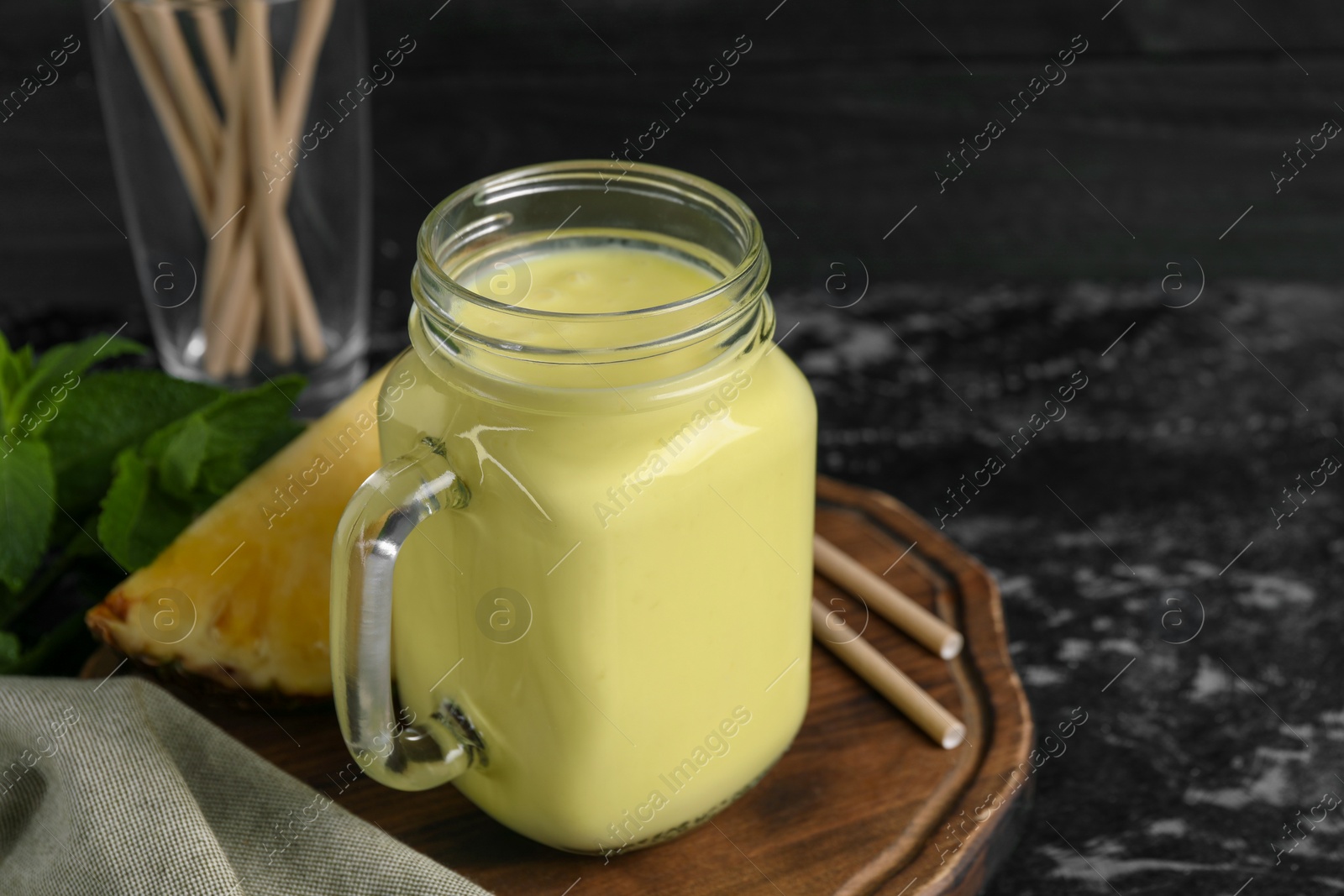 Photo of Tasty pineapple smoothie, mint, slice of fruit and straws on dark textured table. Space for text