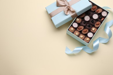 Photo of Open box of delicious chocolate candies and light blue ribbon on beige background, flat lay. Space for text