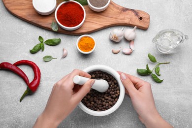 Photo of Woman grinding peppercorns in mortar at light grey table, top view