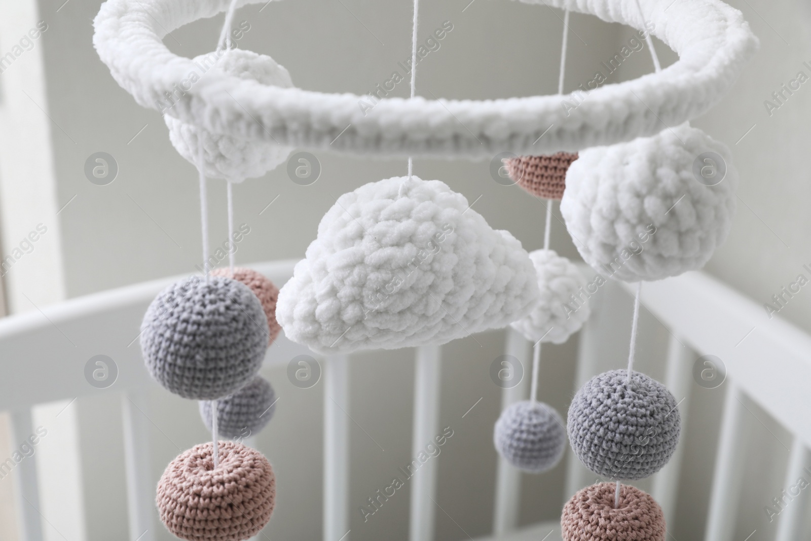 Photo of Modern baby mobile under crib near beige wall in room, closeup