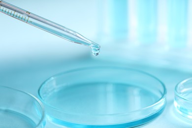 Dripping liquid from pipette into petri dish on blurred background, closeup. Laboratory analysis