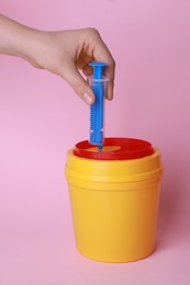 Photo of Woman throwing used syringe into sharps container  on pink background, closeup