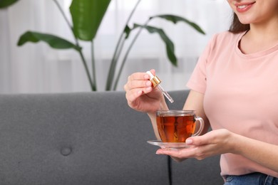 Woman dripping food supplement into cup of tea indoors, closeup. Space for text