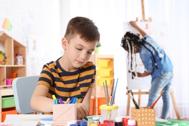 Photo of Cute little child drawing at painting lesson indoors