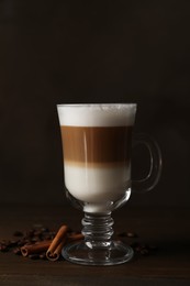 Photo of Hot coffee with milk in glass cup, beans and cinnamon sticks on wooden table