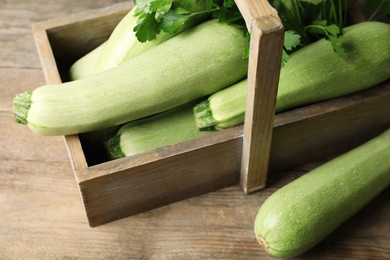 Photo of Crate with ripe zucchinis on wooden table, closeup