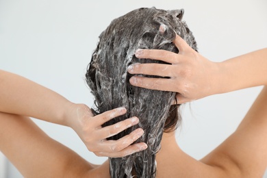 Photo of Woman applying shampoo onto her hair against light background